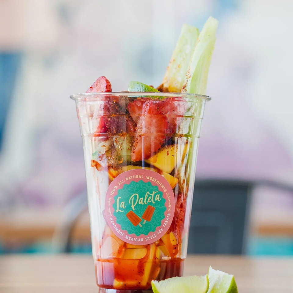 La Paleta fruit cup with strawberries, mango, cucumber, and chili powder, with lime wedges.