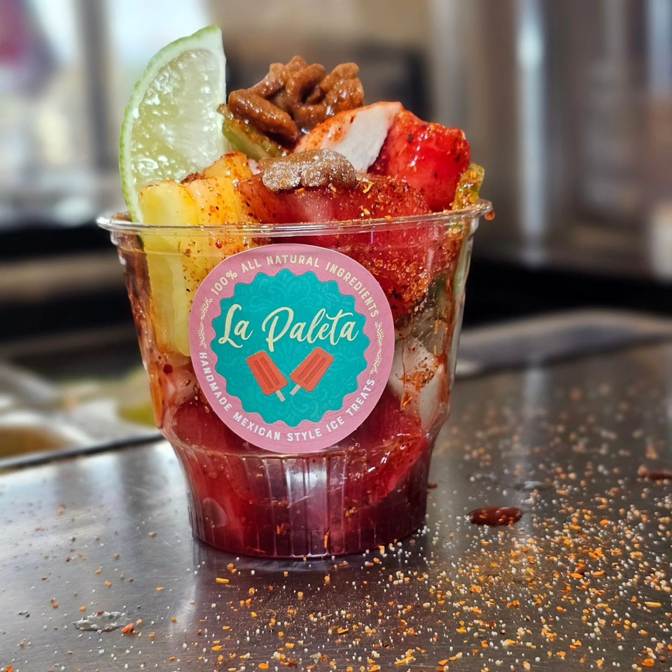 La Paleta's fruit cup with strawberries, pineapple, lime, and tamarind candy on a metal surface.
