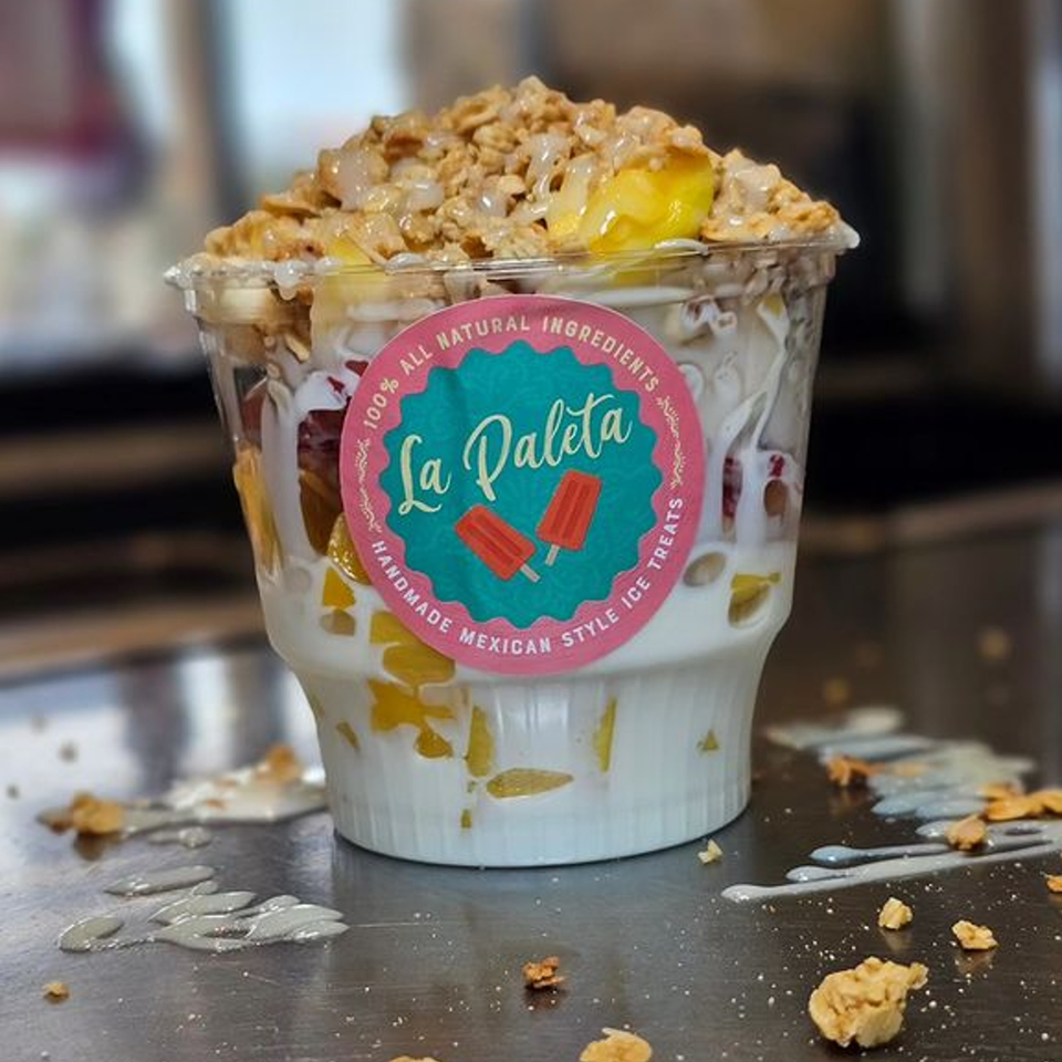 La Paleta dessert cup filled with fruit, cream, and granola, with a pink and teal logo.