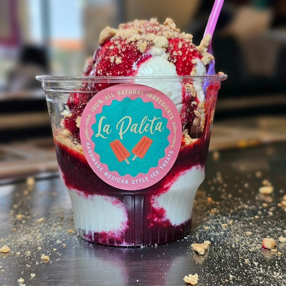 La Paleta dessert cup with white ice cream, red fruit topping, and cookie crumbles.