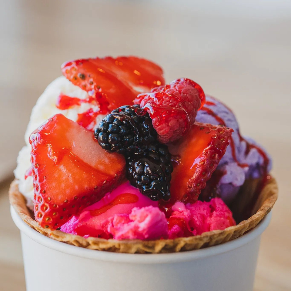 La Paleta's colorful ice cream dessert in a waffle cone cup, topped with fresh berries and syrup.