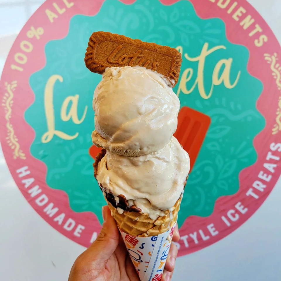 Hand holding a La Paleta waffle cone with two scoops of ice cream and a Lotus Biscoff cookie.