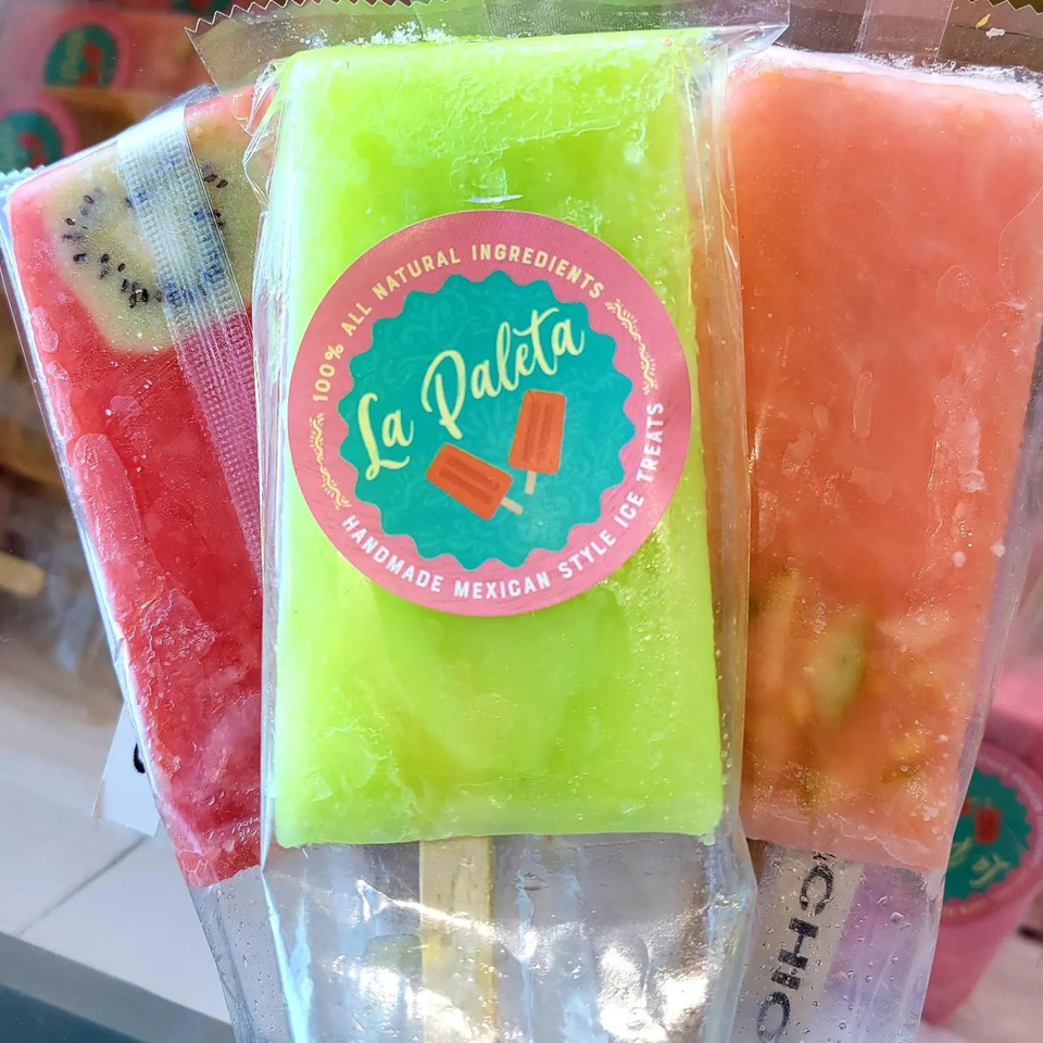 Three La Paleta Mexican-style ice treats, including kiwi, lime, and peach flavors, in clear packaging.